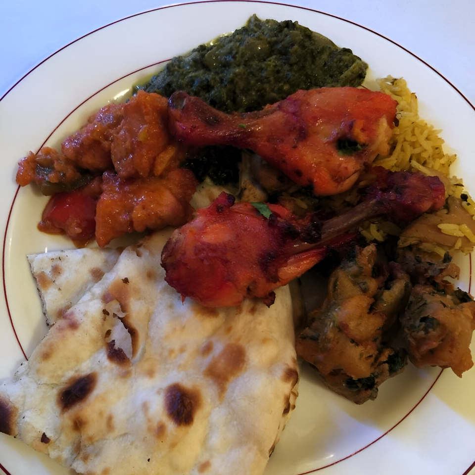 A plate of Amber Indian Restaurant's food, including chicken tikka, saag, rice, chicken curry, and naan.
