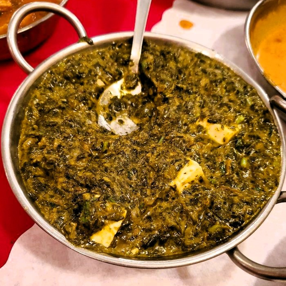 Palak Paneer, a vibrant green Indian spinach and cheese dish, in a metal serving bowl.