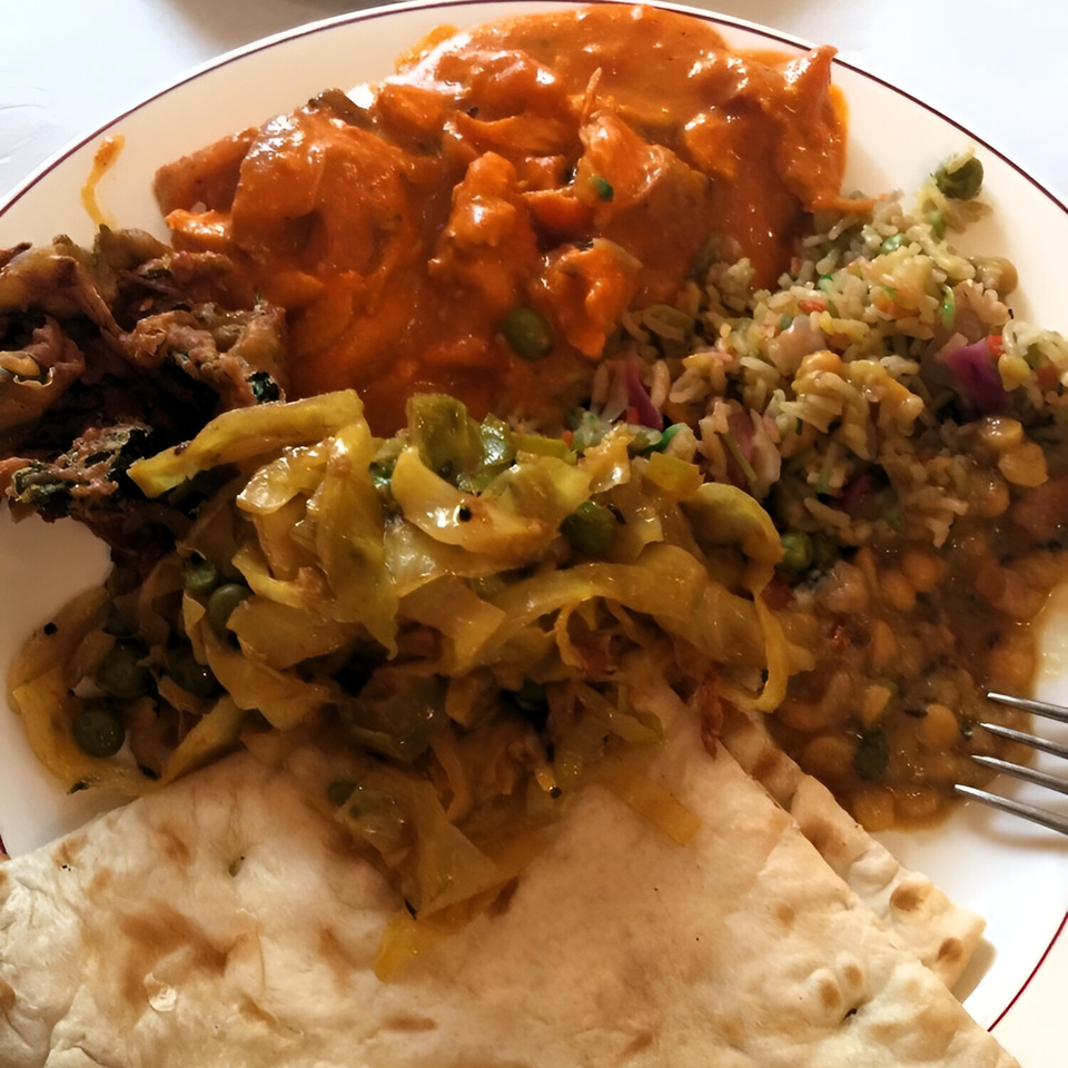 A plate of Amber Indian food with chicken tikka masala, rice, vegetables, and naan.