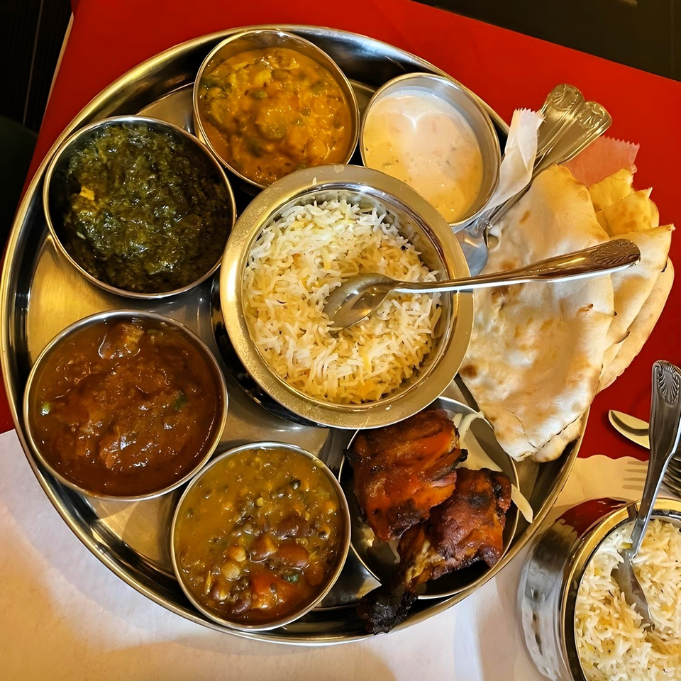 An Indian thali with rice, naan, chicken, spinach, lentils, and other curries on a red table.