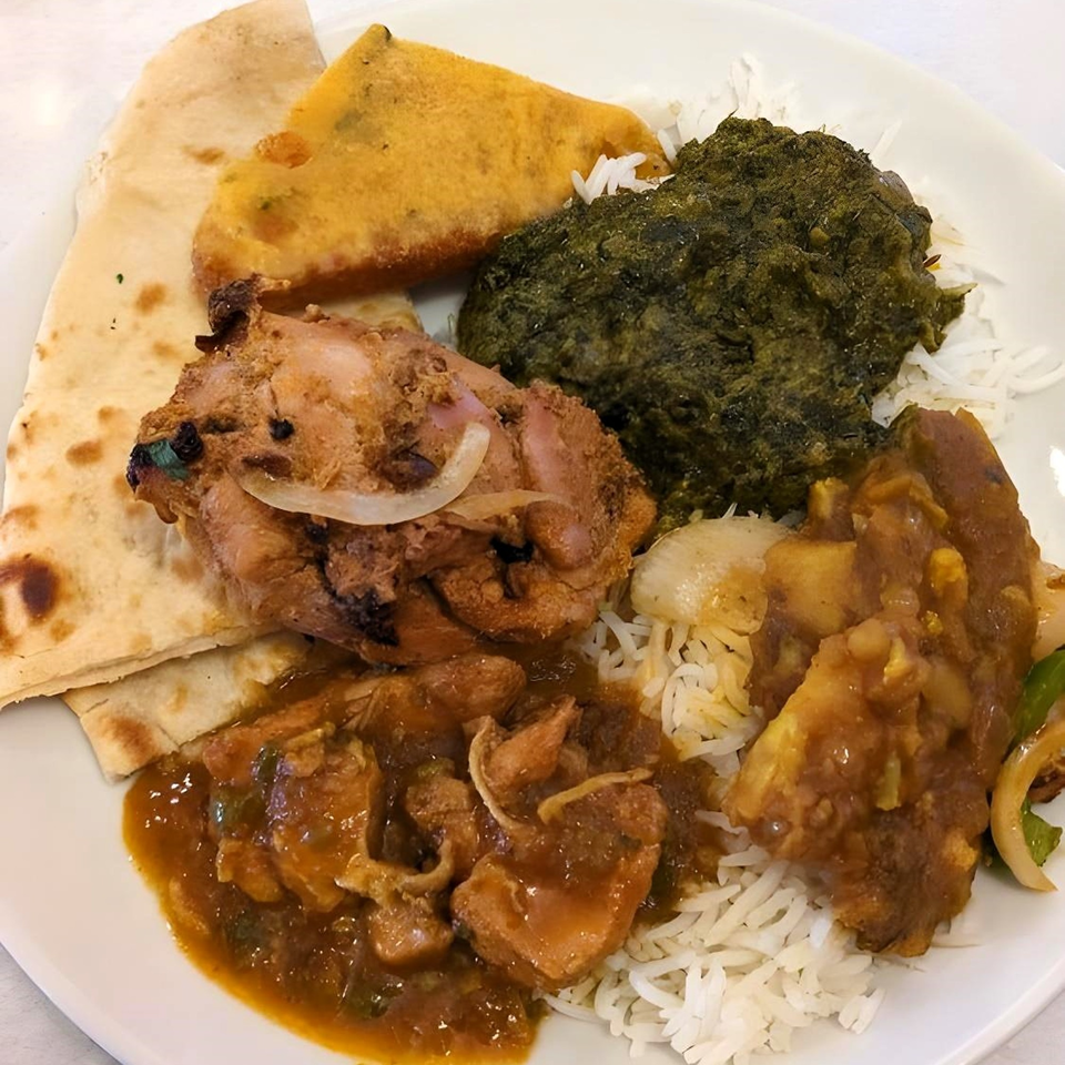 A plate of Amber Indian Restaurant's chicken curry, saag, pakora, and naan with rice.